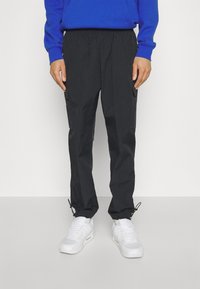 Svarta cargobyxor i lätt material med texturerad yta, utrustade med sidfickor och justerbara dragsnören vid anklarna.