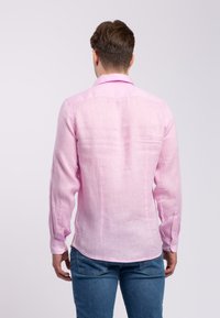 Camicia a maniche lunghe in lino rosa chiaro, con colletto button-down, yoke posteriore e polsini con un solo bottone, mostrata da dietro.