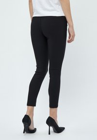 Pantalons noirs slim-fit avec une texture lisse, dotés de poches arrière et d'une taille mi-haute. Associés à des chaussures à talons hauts noires.