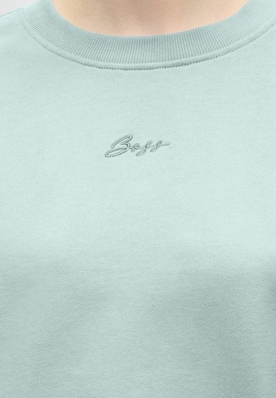 Gros plan d'un sweat-shirt bleu clair à col rond avec un petit logo « Boss » brodé centré sous l'encolure.