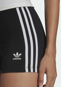 Černé sportovní šortky s třemi bílými pruhy po stranách a malým bílým logem Adidas blízko lemu. Hladká, přiléhavá tkanina.