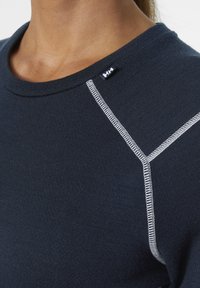 Granatowa dzianinowa koszula z okrągłym dekoltem, kontrastowym białym przeszyciem wzdłuż szwów oraz małą metką z logo blisko kołnierza.