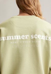 Lichtgroene sweatshirt met witte blokletters "zomerse geuren" en kleinere tekst. Glad textuur met een ronde halsontwerp.