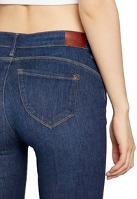 Dark blue denim jeans with a fitted design, featuring a leather branded patch, rear pockets, and contrast stitching.