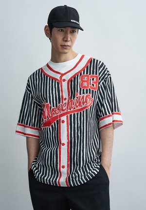 Striped black and white jersey with red accents and buttons, featuring a prominent "Moschino" logo and number "83." Casual fit, short sleeves.