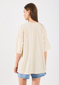 T-shirt oversized bege com mangas curtas e decote redondo, feito de tecido macio. Combinado com calções de ganga desfiados.