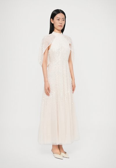 Dlhé svetlé šaty s vysokým golierom a plášťovými rukávmi. Živôtik je zdobený textúrovanými detailmi. Celkový vzhľad dotvárajú saténové mule.