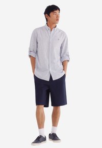 Lichtblauw en witte gestreepte overhemd, gecombineerd met donkerblauwe shorts. Afgewerkt met grijze sneakers en witte sokken.
