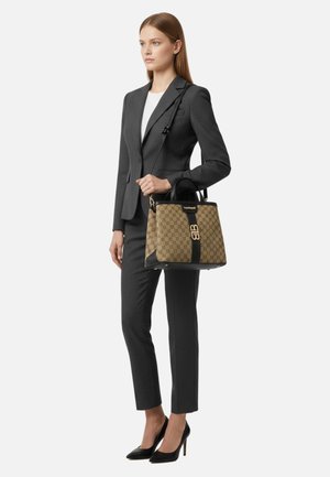 Borsa marrone con motivo a fantasia, dettagli neri, accessori dorati e forma strutturata. La modella indossa un completo grigio su misura e tacchi neri.