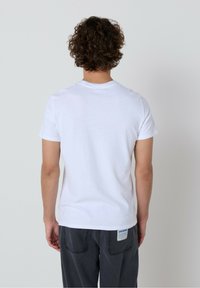 Baltos medvilnės marškinėliai su trumpomis rankovėmis ir apvalia iškirpte, matomi iš nugaros. Turi vienodą dizainą ir laisvą sijoną.