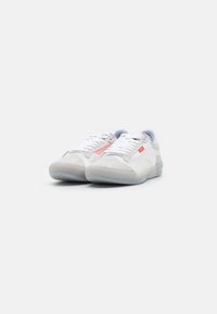 Sneakers brancos com detalhes em cinza e rosa, feitos de materiais em malha e camurça. Apresentam uma sola translúcida e atacadores brancos e planos.