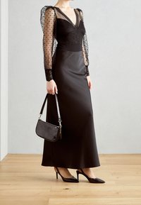 Abito da sera nero con un corpetto lungo a maniche trasparenti e puntinate, abbinato a una gonna in seta lucida. Completo con una piccola borsa nera e tacchi a punta.