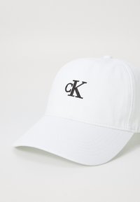 Witte baseballcap van katoen met een gebogen klep. Heeft een geborduurd "cK" logo in het zwart aan de voorkant.