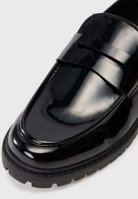 Svarta Lackläder loafers med en slät, glänsande yta, med ett brett band över framsidan och en grov texturerad sula.