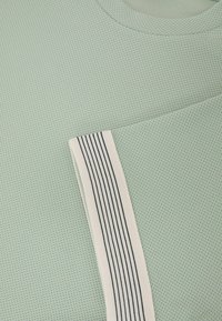 Tissu vert menthe texturé avec un motif hexagonal, comportant un accent rayé blanc et noir sur un bord du vêtement.