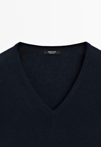 Pull col en V bleu marine en matière douce, présentant une texture lisse et un design simple, avec une étiquette noire visible au niveau de l'encolure.