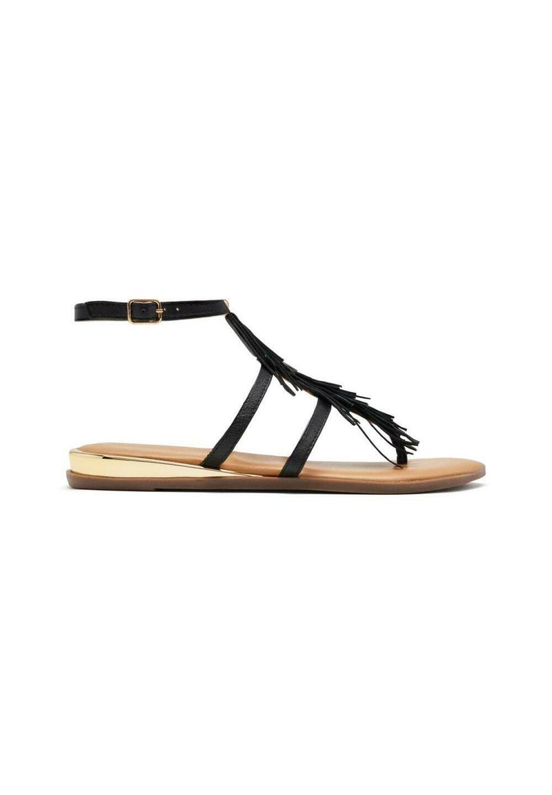 Sandalia gladiadora de cuero negro con detalles de flecos, correa ajustable en el tobillo y suela plana en tonos marrones con acento metálico.