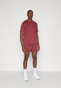 Camiseta de algodón roja y pantalones cortos a juego con un corte relajado. Usados con zapatillas blancas y calcetines hasta el tobillo. Diseño sencillo, sin patrones visibles.