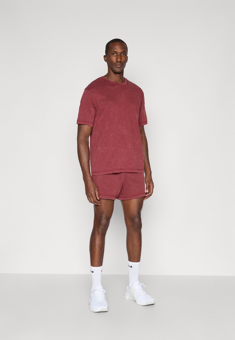 Rotes Baumwoll-T-Shirt und passende Shorts mit lockerem Schnitt. Getragen mit weißen Sneakern und Knöchelsocken. Schlichter Entwurf, keine sichtbaren Muster.