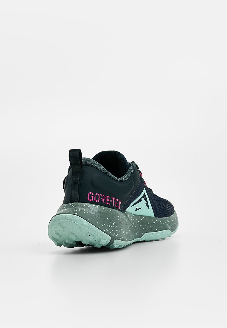 Zapatilla deportiva azul marino con parte superior de tejido texturizado, logo rosa "GORE-TEX" y suela exterior verde claro salpicada. Cuenta con una lengüeta para facilitar su puesta.