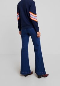 Sudadera azul marino con acentos a rayas multicolores en las mangas, combinada con jeans de tiro acampanado de color azul oscuro. Tejido suave y un ajuste casual.