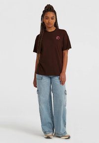 Brun bomuld t-shirt med korte ærmer og en lille pink logo, kombineret med lyseblå vidde cargobukser med sidelommer.