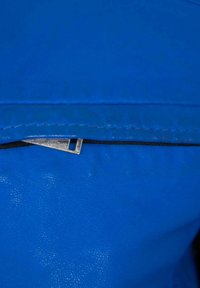 Blaues Leder mit glatter Textur, ausgestattet mit einem Metallreißverschluss und genähnten Kanten. Nahaufnahme des Reißverschlussbereichs.