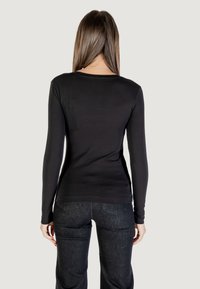 Maglietta nera a maniche lunghe con collo rotondo, texture liscia e design aderente, abbinata a jeans denim scuri.