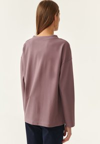 Dlhý rukáv, voľný strih vrch s utišenou mauve bavlnou. Má okrúhly výstrih, rovný lem a minimalistický dizajn bez vzorov.