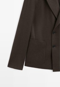 Brązowa wełniana marynarka o fakturowanym wykończeniu, z klapą z nacięciem, pojedynczą kieszenią i czarnymi guzikami z przodu.