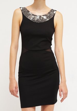 Sleeveless black dress with beaded silver neckline and sheer side panels worn by a standing woman against a plain background.