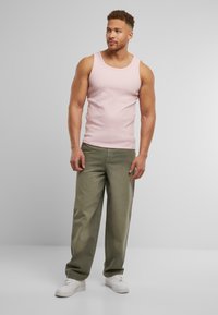 Lyserød tanktop, løse olivengrønne bukser, hvide sneakers. Modellen står på en grå baggrund. Blød, glat stoftekstur.