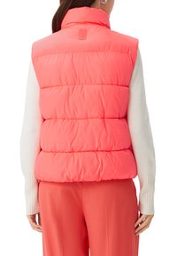 Puffweste in leuchtendem Neonpink mit hohem Kragen und gesteppten Paneelen. Getragen über einem weißen Langarmoberteil mit gerippten Bündchen.