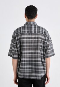 Camicia a maniche corte con design a quadri in nero, bianco e grigio; presenta una vestibilità rilassata, colletto e un yoke posteriore per una maggiore struttura.