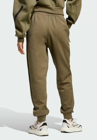 Olivové joggers s elastickým pásom, rebrovanými manžetami a bočnými vreckami, skombinované so svetlými športovými topánkami.