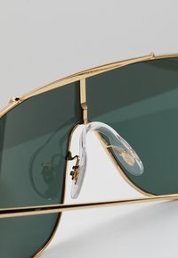 Occhiali da sole in metallo dorato con grandi lenti verdi, dotati di doppio ponte e naselli trasparenti per il comfort. Finitura lucida e design elegante.
