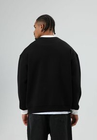 Zwarte oversized sweatshirt met verlaagde schouders en geribbelde manchetten. Voorzien van een contrasterende witte binnenkant van de halslijn. Zachte stoftextuur.