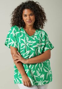 Blusa corta de manga corta verde con estampados florales blancos, diseño de escote en V, corte relajado y textura suave, adecuada para uso casual.