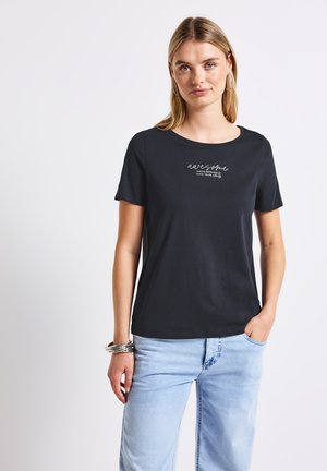 T-shirt en coton noir à manches courtes, col rond et impression "super" sur le devant. Porté avec un jean bleu clair.