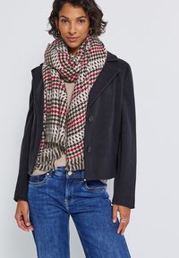 Sort cropped jakke, beige striktrøje, blå jeans og et mønstret tørklæde i beige med røde og sorte accenter. Fringed tørklæde detalje synlig.