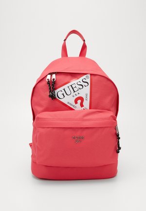 Sac à dos rouge Guess avec tirettes de fermeture éclair noires, poche avant et grand logo triangulaire blanc avec le texte « GUESS » et un point d'interrogation rouge.