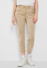 Jeans cortos beige de corte slim, con bolsillos frontales, cierre de botón y detalles de costura sutiles. Combinados con zapatillas blancas.