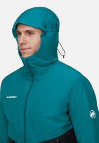 Teal Mammut jakke med hætte, der har en glat tekstur, en lynlåslukning foran og logo detalje på ærmet. Justerbar snor ved hætten.