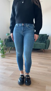 Λεπτά τζιν σε μπλε απόχρωση με κανονική μέση, συνδυασμένα με κοντό μαύρο πλεκτό πουλόβερ. Μαύρες λόφερ με χρυσές λεπτομέρειες.