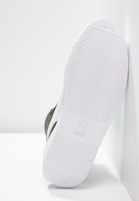 Svart och vit sneaker med strukturerad gummisula, med ett zigzag-mönster; varumärkeslogotyp präglad på hälen.