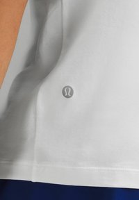 Hvid bomulds T-shirt med rund kant, korte ærmer og et diskret logo i grå på nederste højre side. Blød tekstur.