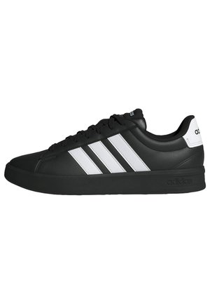 Zapatilla negra de Adidas con tres franjas blancas en los laterales, suela negra y lengüeta trasera blanca con el logo de Adidas.