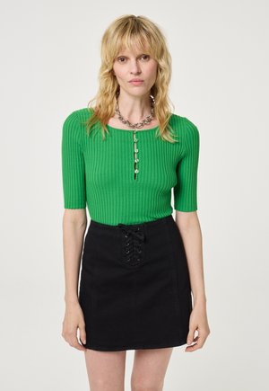 Groene geribbelde top met korte mouwen en een ronde halslijn, vergezeld van een zwarte mini-denimrok met een voorste vetersluiting.