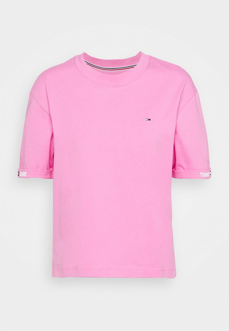 Camiseta rosa de manga corta con pequeño logo de Tommy Jeans en el pecho y la marca Tommy Jeans en blanco en los puños de las mangas.