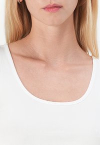 Witte, scoop-neklijn tanktop van gladde, aansluitende stof. Heeft een lage halslijn en minimale stiksels rondom de randen.